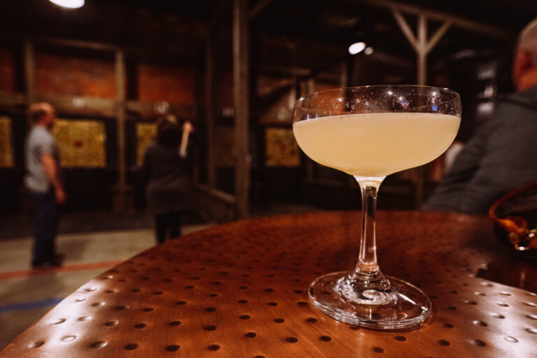 an attractive cocktail with our axe throwing lounge in the background